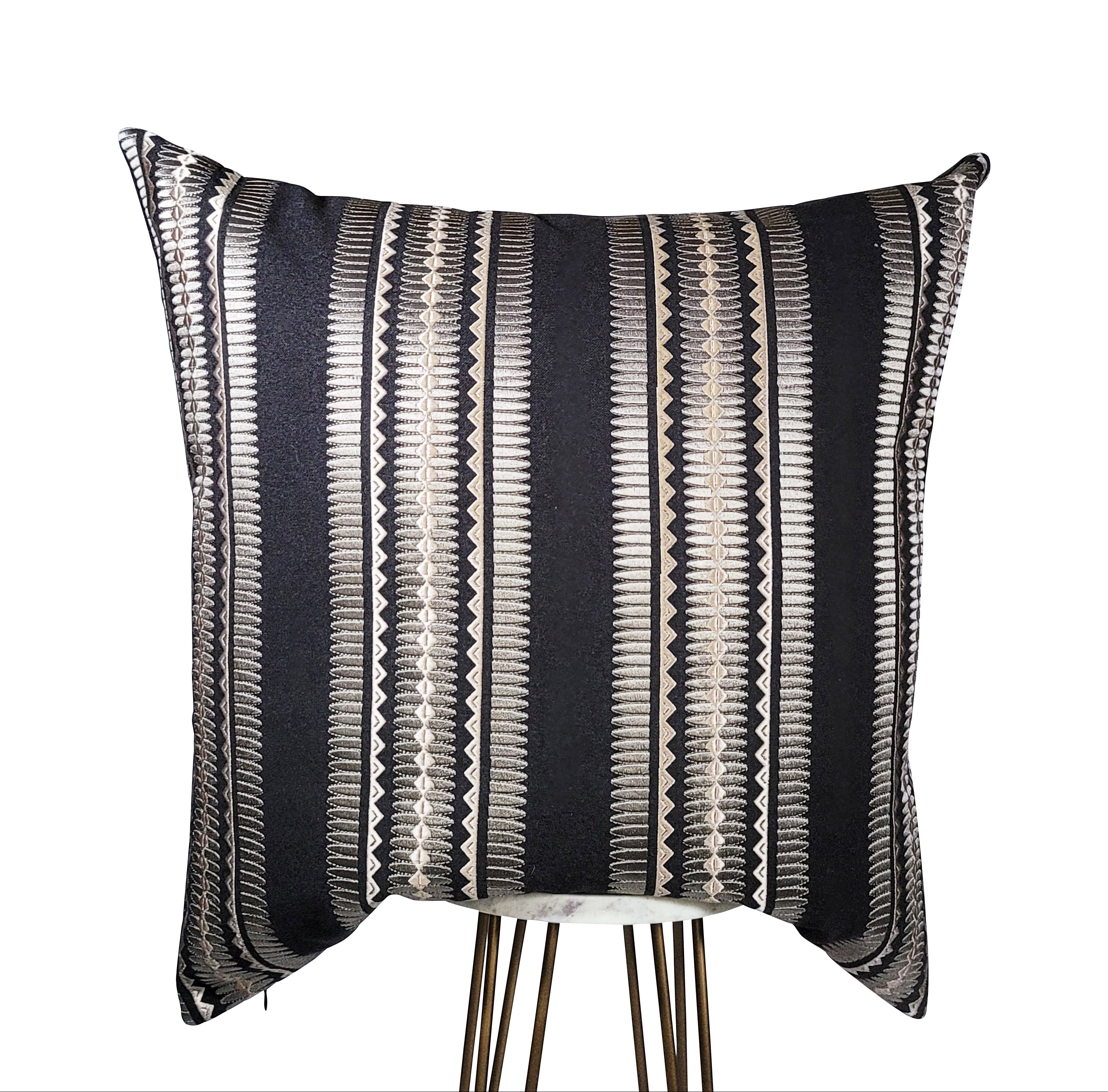 A rectangular pillow with a black base featuring a geometric pattern of silver accents and pink highlights.