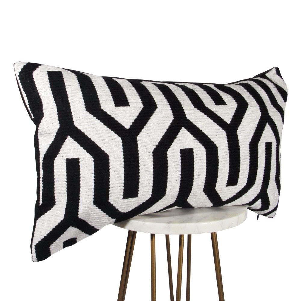 side-view of a black and white 13x21 rectangle throw pillow with large geometric design throughout, displayed on small white table.