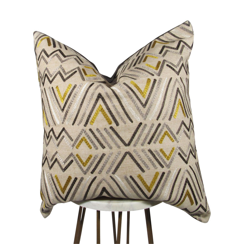 A square-shaped throw pillow with a geometric pattern featuring stripes in taupe, gray, and gold colors, showcased on a simple background.