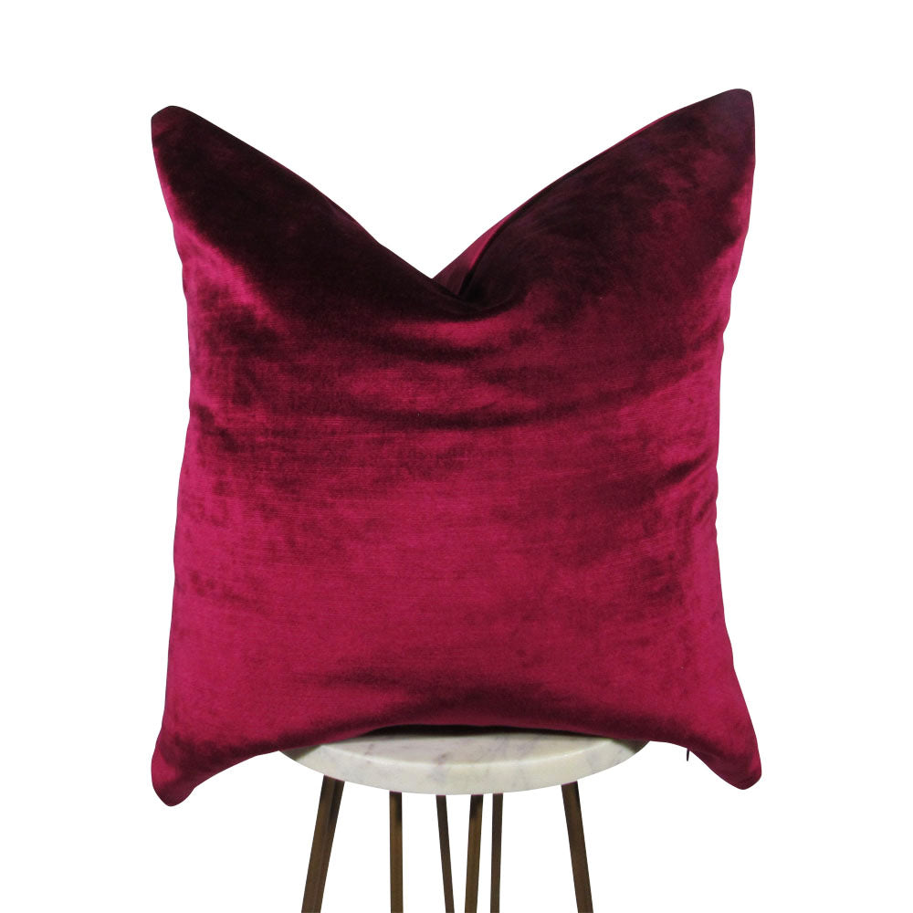 A raspberry red velvet pillow with a hidden zipper, displayed on a simple white stand.