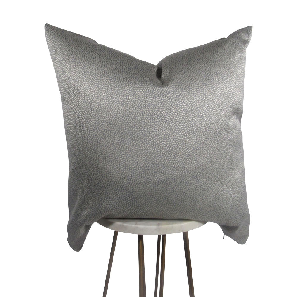 A slate gray dot pillow with a hidden zipper, displayed on a simple wooden stand.
