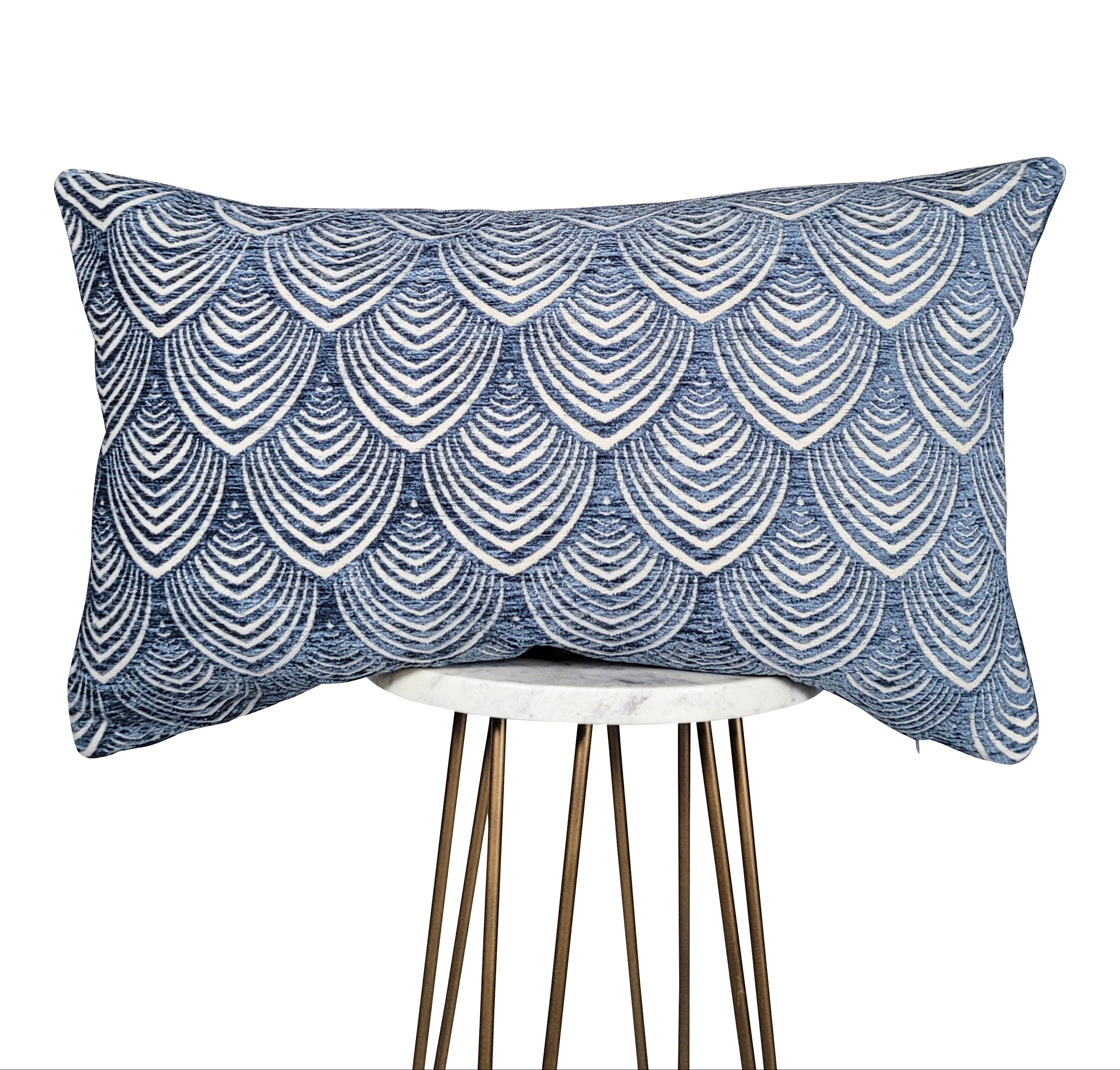 A light blue and cream scallop pattern fabric throw pillow, displayed on a simple stool.