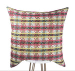 A square-shaped pink pillow with a geometric pattern featuring stripes in fuchsia, green, white, and blue colors.