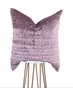 A rectangular-shaped mauve and gray geometric-patterned pillow with a velvet texture, displayed on a stand against a white background.