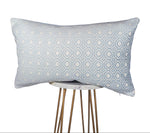 A powder blue and white quatrefoil patterned pillow on a wooden four-legged stool.