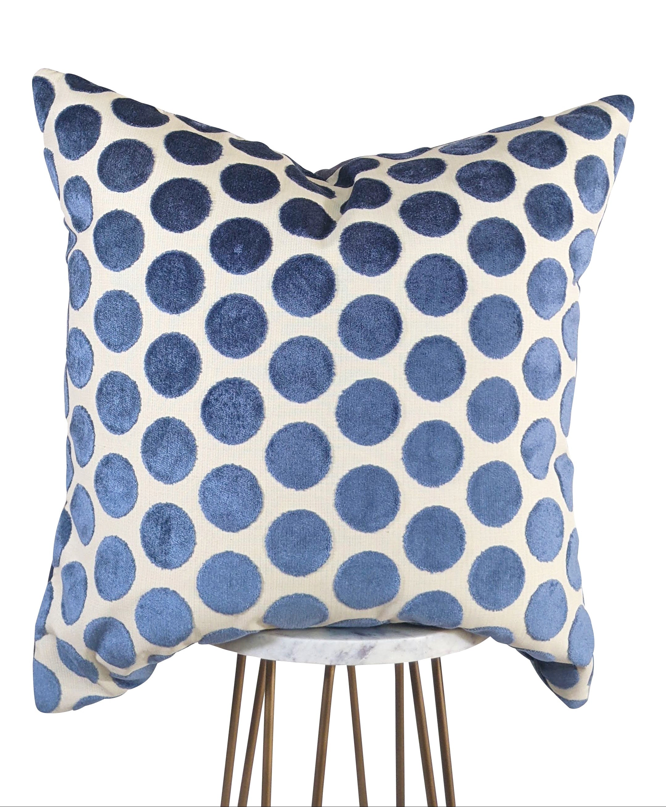 A baby blue polka dot pillow with a creamy white background, displayed on a metal stool.