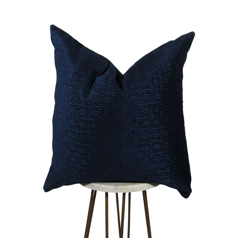shiny royal blue square throw pillow with geometric designs throughout. displayed on small white circle table.
