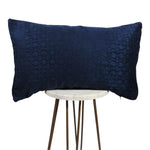 shiny royal blue lumbar throw pillow with geometric designs throughout. displayed on small white circle table.