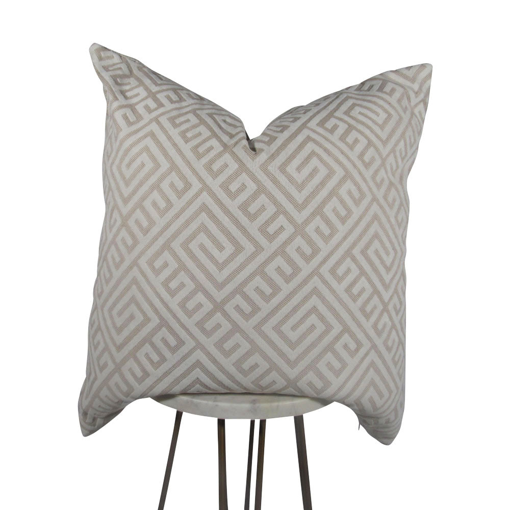 A beige throw pillow with a geometric Greek key pattern, placed on a table.