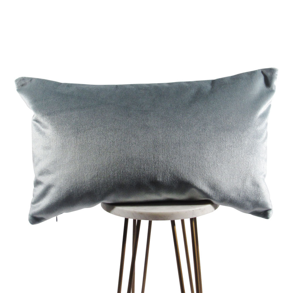 A rectangle-shaped, solid blue velvet throw pillow with a hidden zipper closure, placed on a modern style wooden stool.