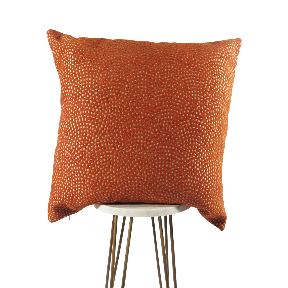 An orange and cream orange geometric patterned pillow cover, displayed on a table with a simple metal frame.