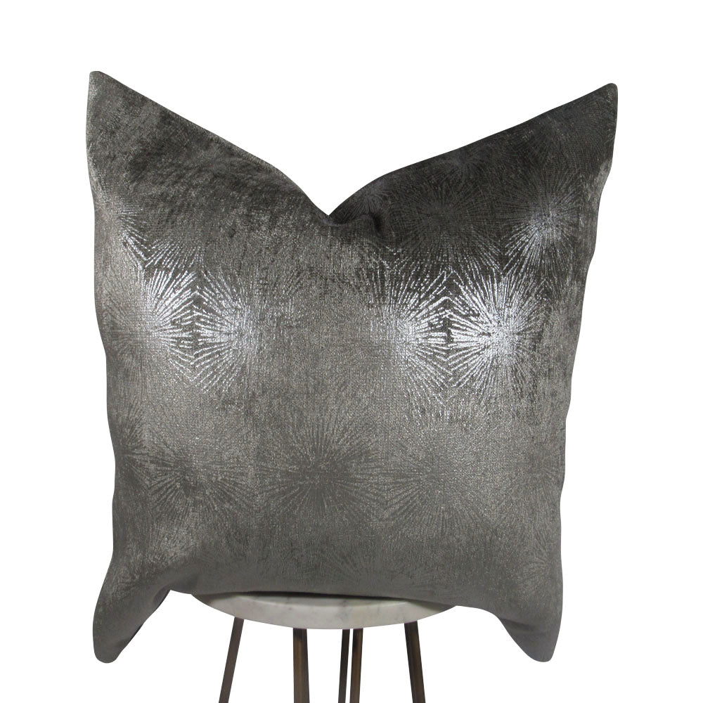 A light gray throw pillow with a silver sunburst pattern, displayed on a stand.