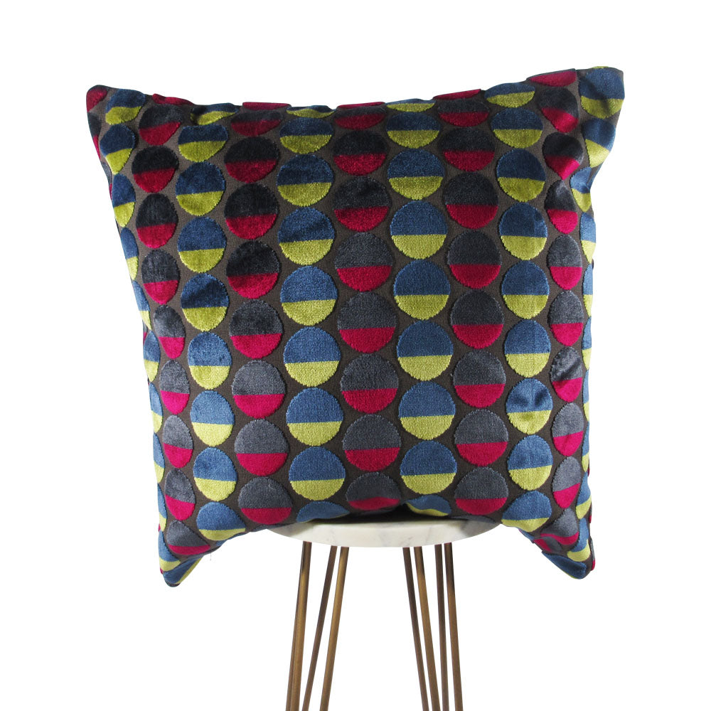 A multicolored round throw pillow with a polka dot pattern, predominantly featuring yellow, red, and blue shades, placed on a tripod stand.