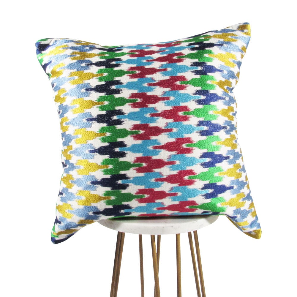 A multicolored geometric patterned jigsaw puzzle pillow in blue, green, red, and yellow shades, placed on a chair.